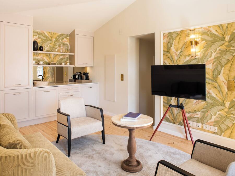 Uma sala de estar moderna com sofá, cadeiras, mesa de centro, televisão em um móvel e área de cozinha com armários e bancada.