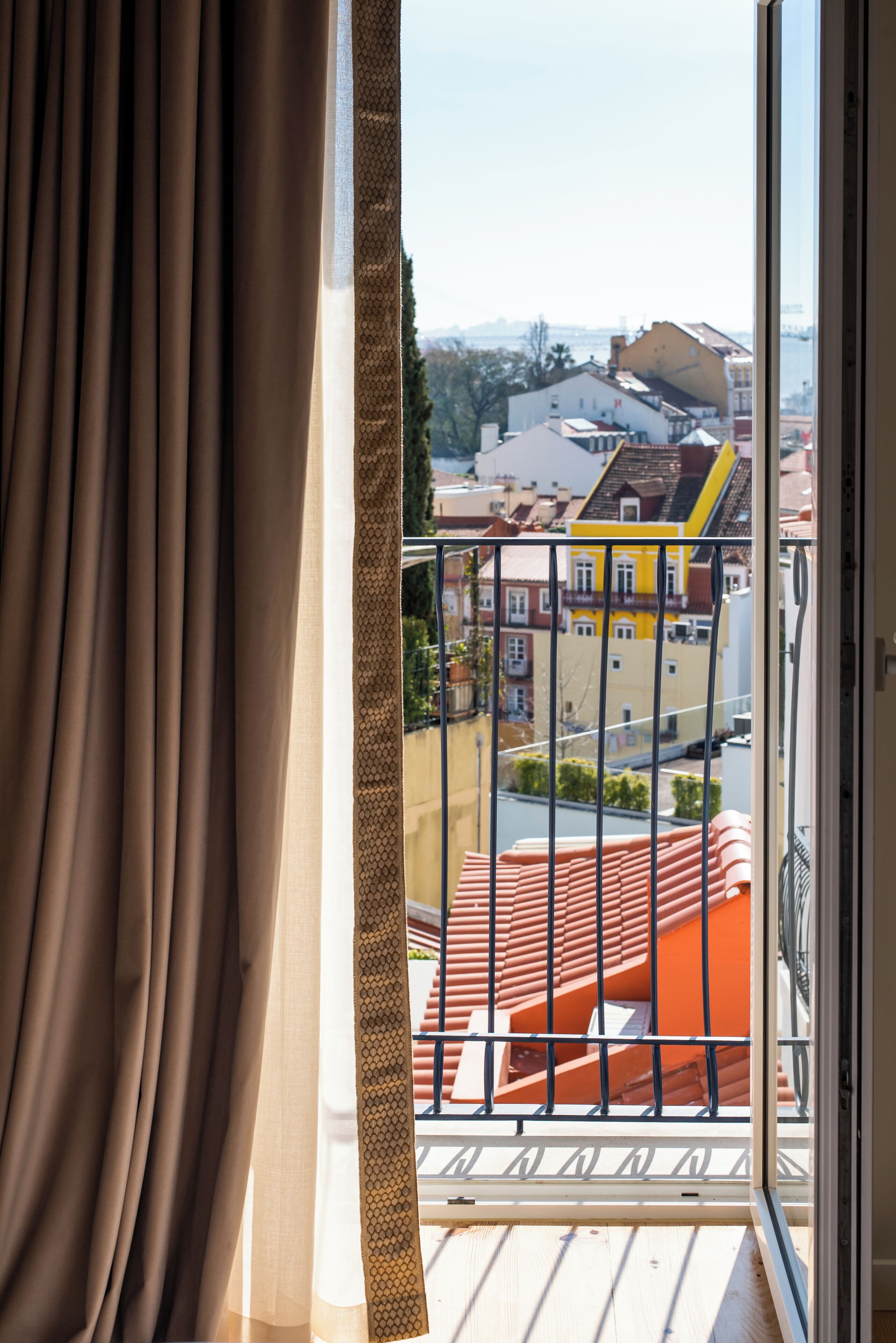 Een balkon met uitzicht op kleurrijke gebouwen, een balustrade en een gedeeltelijk open gordijn.