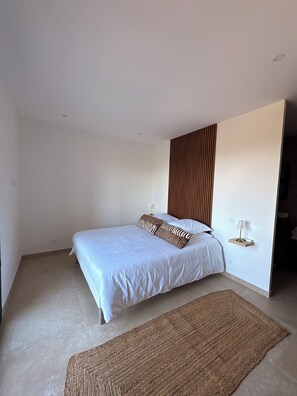 Ein Schlafzimmer mit einem Bett, einer Holzwand, einem Nachttisch mit Lampe und einem gewebten Teppich.