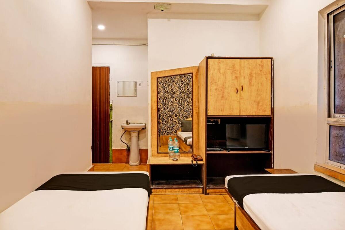 Quarto de hotel com duas camas, guarda-roupa de madeira, pia e televisão.