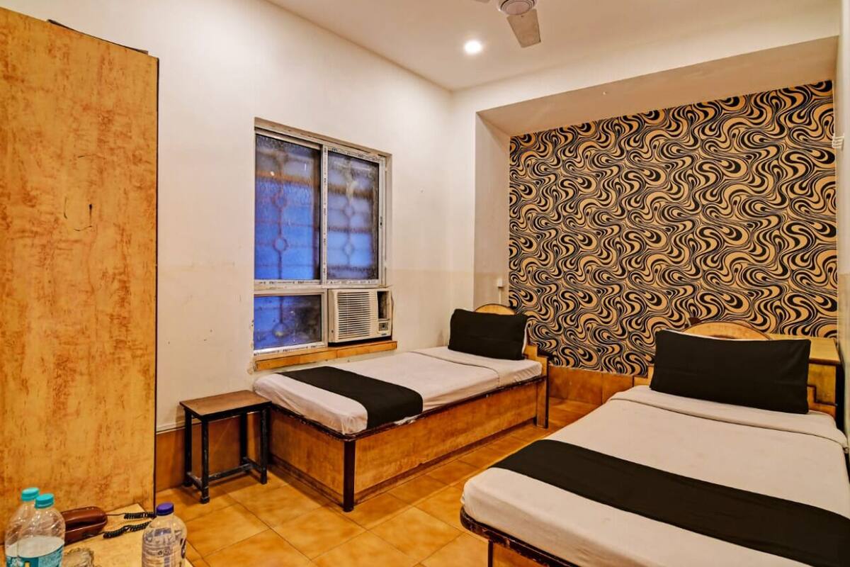 Quarto com duas camas, janela com vidro fosco, aparelho de ar condicionado e parede com padrão.