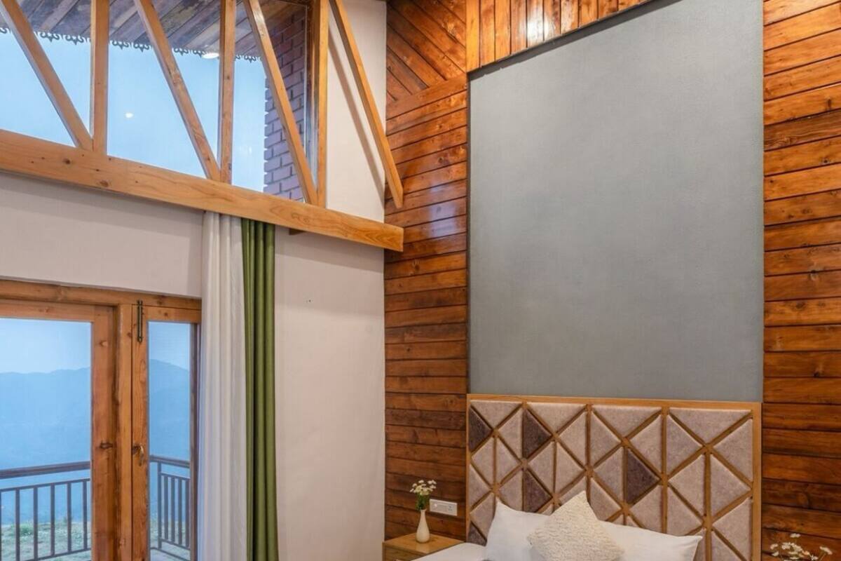 A bedroom with a wooden ceiling, a large bed with a headboard, a nightstand, and a view through a glass door.
