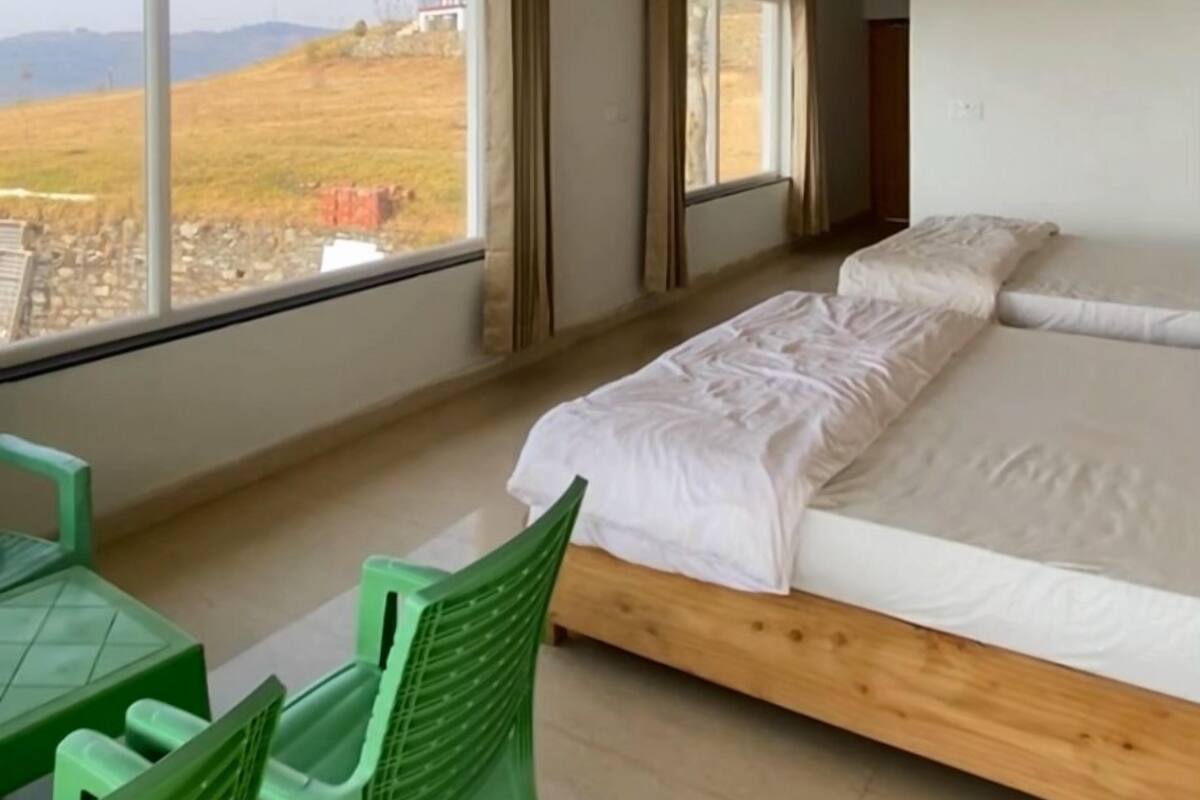 A bedroom with a wooden ceiling, a bed, a window, and a view of a grassy field.
