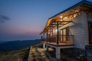 Ein zweistöckiges Haus mit Balkon, einer Holzterrasse und einem Steinfundament.