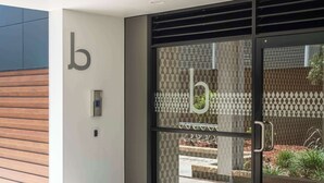 A modern building entrance with a glass door, a 'b' logo, and a metal handle. - Elite Escape - Absolute Beachfront Luxury (Newcastle)