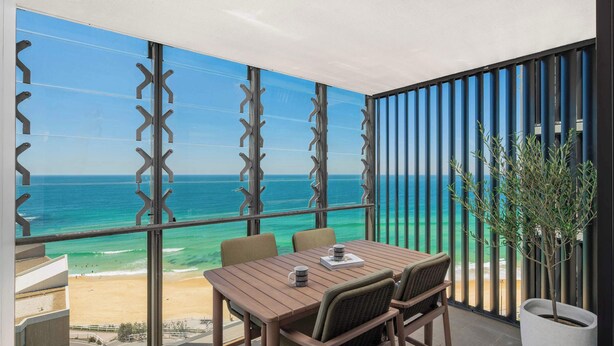 A balcony with a wooden table and chairs, a potted plant, and a view of the beach and ocean. - Elite Escape - Absolute Beachfront Luxury (Newcastle)
