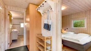 Un interno in legno con un letto, una mensola, una borsa appesa e una finestra vista.