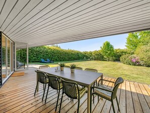 An outdoor patio with a wooden table and chairs, a glass door leading to a garden, and a view of a well-maintained lawn and trees. - "Yorick" - 350m to the fjord by Interhome (Tarm)