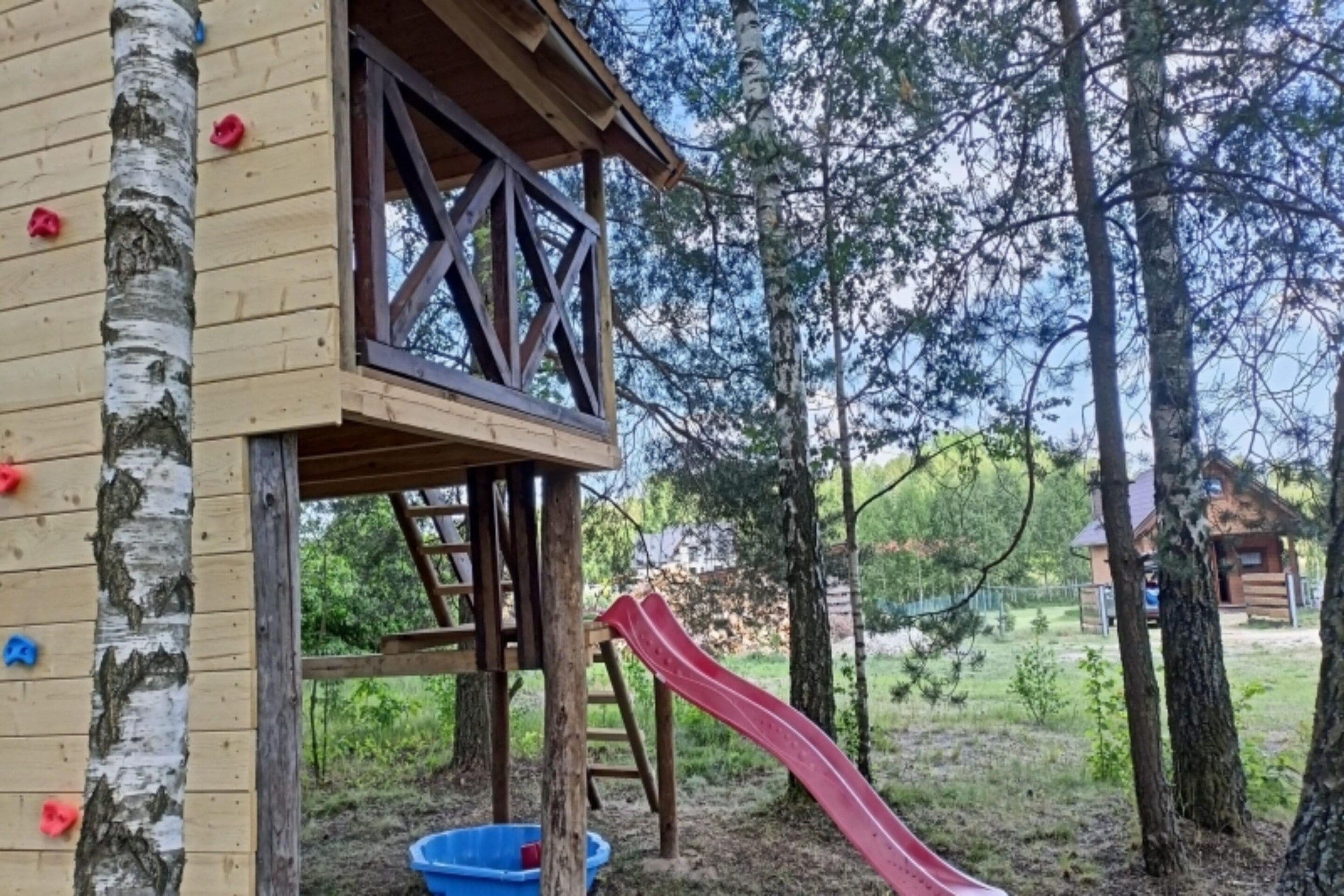 A wooden play structure with a slide, climbing wall, and a blue plastic container.