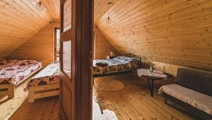 A cozy attic bedroom with wooden walls and a sloped ceiling. There is a bed with a floral bedspread, a small table with a vase, and a sofa. - Holiday Home With Sauna, Jacuzzi and Private Pond (Lipusz)