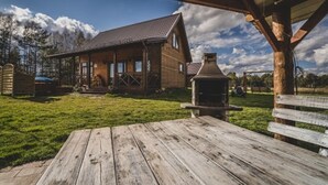 A rustic wooden cabin with a porch, a barbecue grill, and a grassy yard. - Holiday Home With Sauna, Jacuzzi and Private Pond (Lipusz)