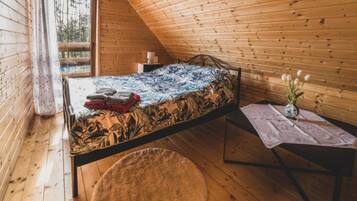 A single bed in a cabin with a wooden ceiling and walls, a small bedside table with a vase of flowers, and a window with curtains.