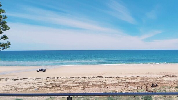 Una spiaggia con un veicolo parcheggiato sulla sabbia, cielo sereno e mare calmo.