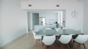 Una cucina moderna con mobili bianchi, un frigorifero in acciaio inossidabile e un forno integrato. C'è una zona pranzo con un tavolo grande e sedie bianche.