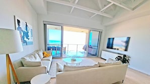Un soggiorno moderno con divano, tavolino e televisione. È presente un balcone con vista sul mare.