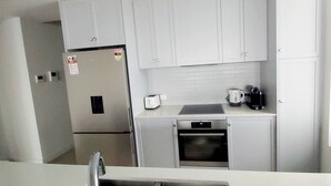 Una cucina compatta con pensili bianchi, forno integrato, tostapane e bollitore sul piano di lavoro.