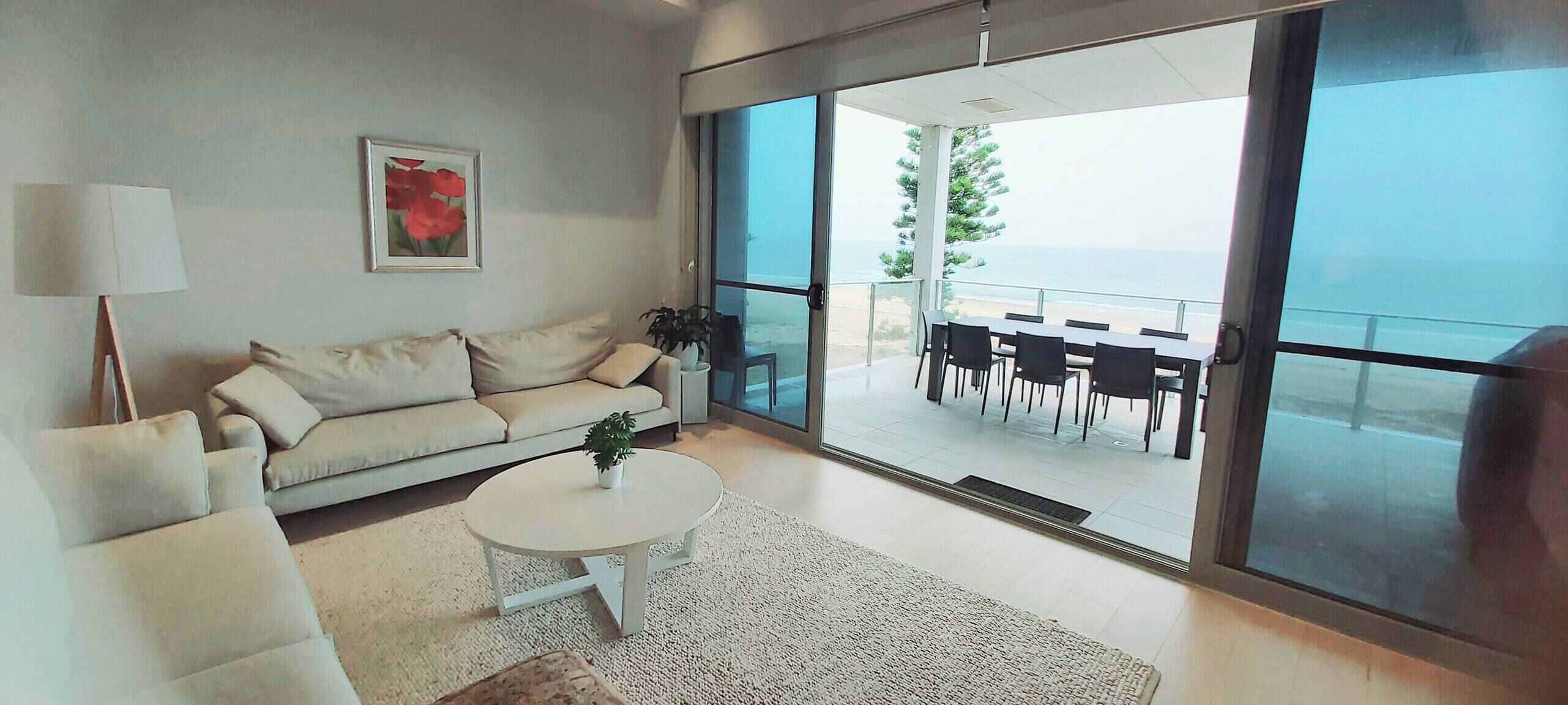 A modern living room with a sofa, a coffee table, and a view of the balcony with outdoor seating.