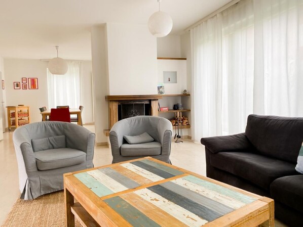 Una sala de estar con dos sillones grises, un sofá negro y una mesa de centro de madera con diseño de retazos.