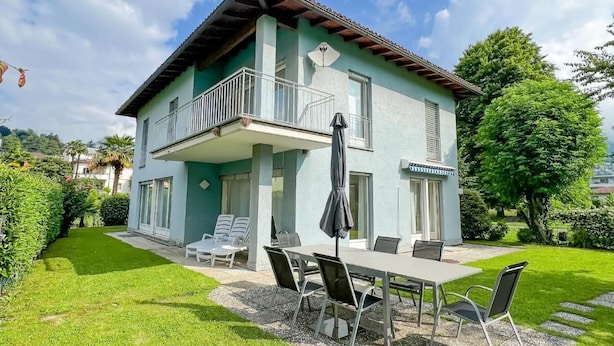 A two-story house with a balcony, a patio with outdoor furniture, and a well-maintained garden.