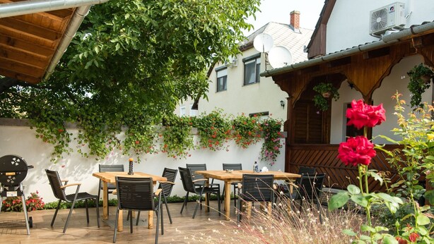 An outdoor patio with a wooden table and chairs, surrounded by greenery and flowers. - mit Swimmingpool für 10 Personen by Interhome (Balatonkeresztur)