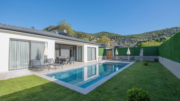 Ett modernt hus med en swimmingpool, en uteplats med stolar och utsikt över de omgivande kullarna.