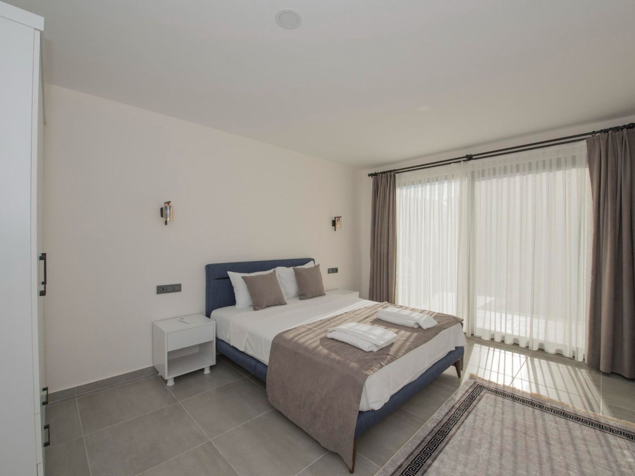 A modern bedroom with a bed, nightstand, and a large window with curtains.