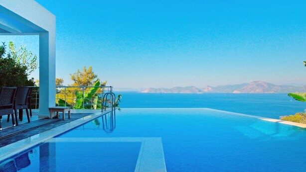Una piscina a sfioro moderna con vista libera sul mare e montagne in lontananza.