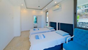 Camera d'albergo con due letti, un'ampia finestra e una poltrona blu.
