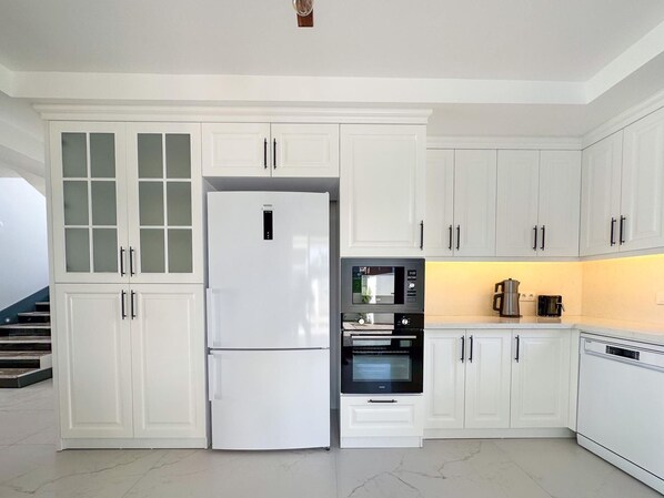 A modern kitchen with white cabinetry, a refrigerator, a microwave, an oven, and a dishwasher.