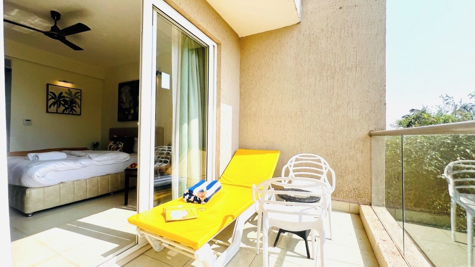 A balcony with a yellow sun lounger, a white chair, and a bed with a white headboard.