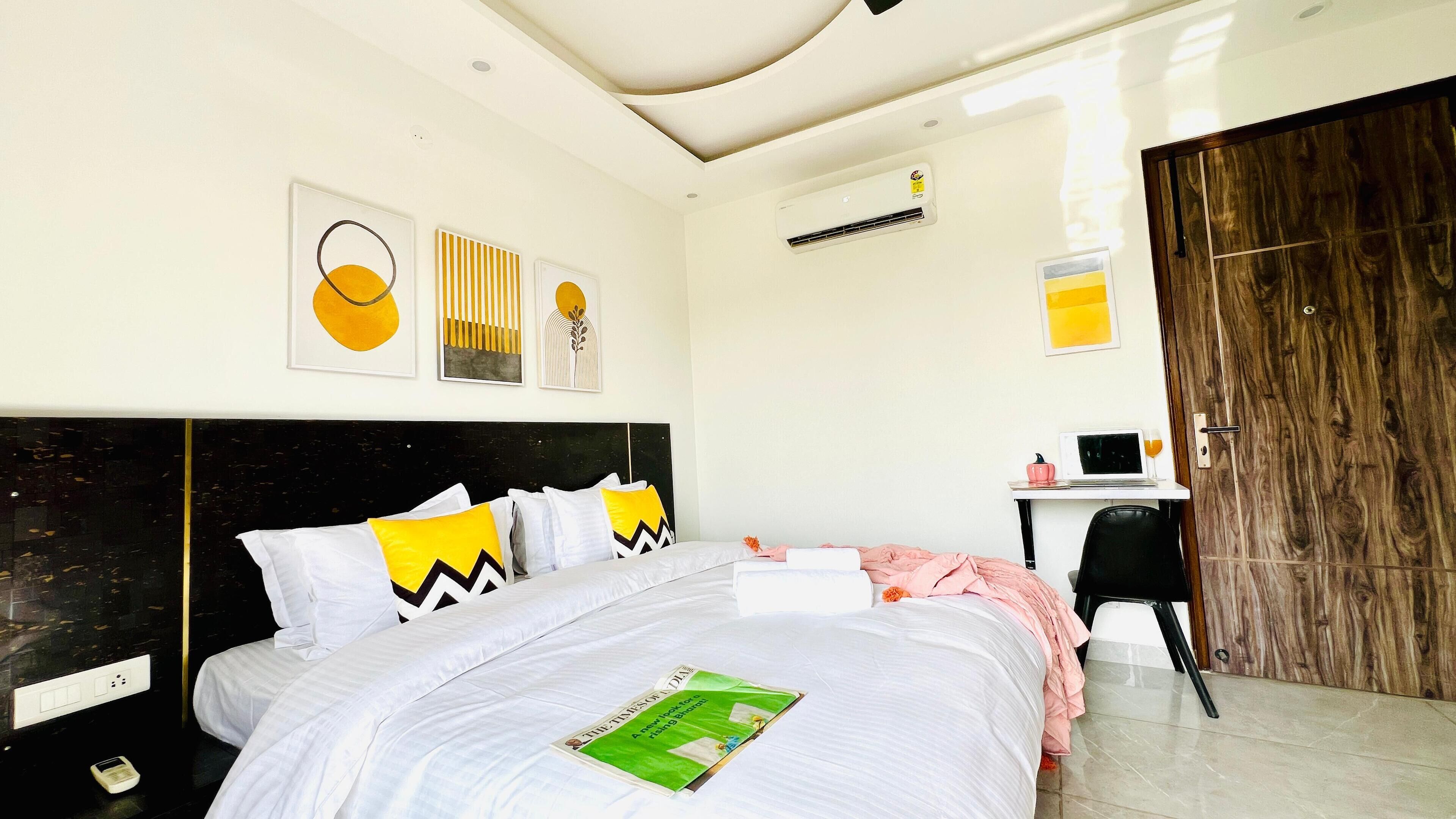 A modern hotel room with a large bed, a desk with a laptop, and a wardrobe.