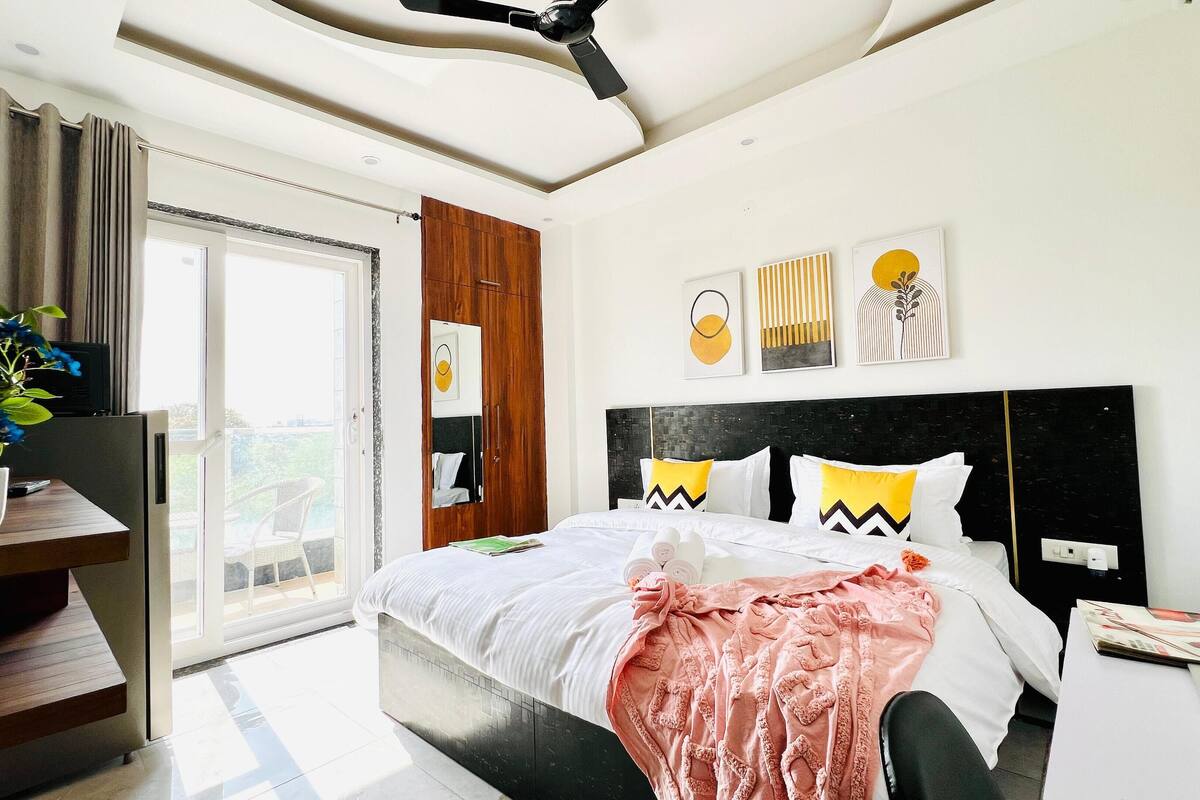 Een moderne hotelkamer met een bed, een bureau, een kamerplant en uitzicht op het omliggende landschap.
