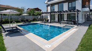 Una casa moderna de dos pisos con piscina, mobiliario exterior y una pérgola.
