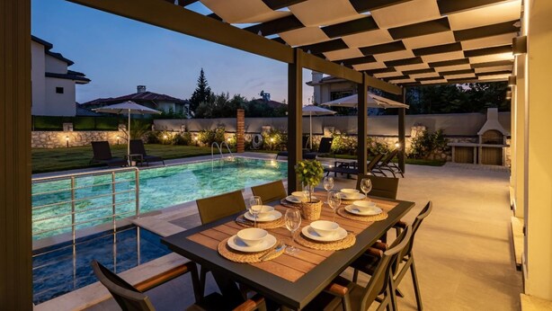 Un espacio de comedor al aire libre con piscina, mesa y sillas de madera.