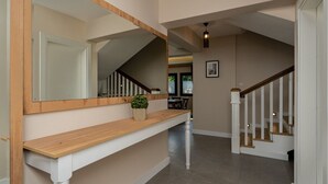 Un pasillo con una consola de madera, una planta en maceta, una escalera con barandillas blancas y un candelabro.