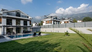 Una zona residencial moderna con piscina, casas de dos pisos y un paisaje montañoso de fondo.