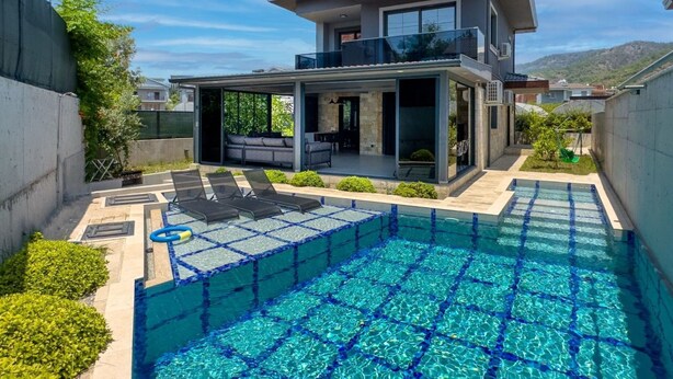 Ein modernes, zweistöckiges Haus mit Swimmingpool, Sitzgelegenheit im Freien und überdachter Terrasse.