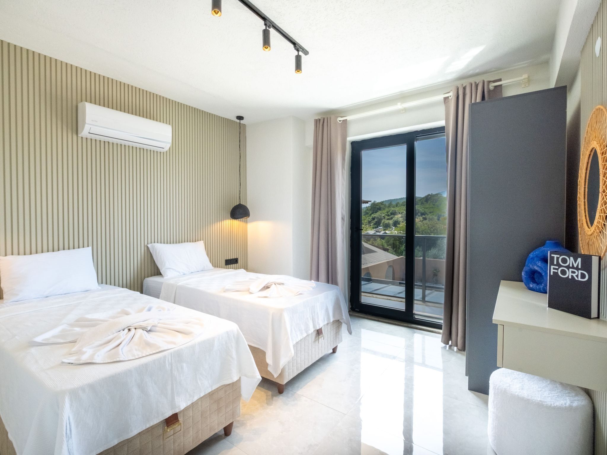 Ett hotellrum med två sängar, en luftkonditioneringsanläggning, ett skrivbord med en lampa, utsikt över omgivningarna och en skylt med namnet ”TOM FORD”.
