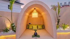 A cozy, semi-enclosed seating area with a cushioned bench, a decorative frog sculpture, and a hanging light fixture.