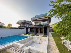 Una casa moderna de dos pisos con piscina, mobiliario exterior y un jardín cuidado.