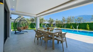 A modern outdoor dining area with a pool, a hanging chair, and a view of the mountains. - Villa in der Natur by Interhome (Ölüdeniz)