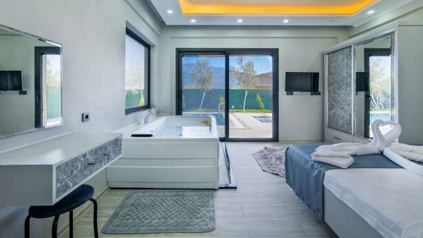 A modern bedroom with a large bed, a vanity with a mirror, a bathtub, and a sliding glass door leading to a balcony. - Villa in der Natur by Interhome (Ölüdeniz)
