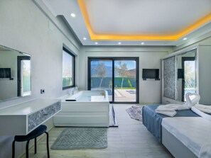 Un dormitorio moderno con una cama grande, un tocador con espejo, una bañera y una puerta corrediza de vidrio que da a un balcón.