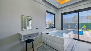 A modern bathroom with a large bathtub, a mirror, and a window overlooking a pool area. - Villa in der Natur by Interhome (Ölüdeniz)