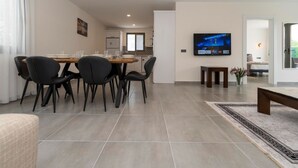A modern living room with a dining area, a TV mounted on the wall, and a view into the kitchen.