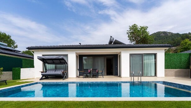 A modern house with a swimming pool, a covered outdoor seating area, and a view of the surrounding landscape.