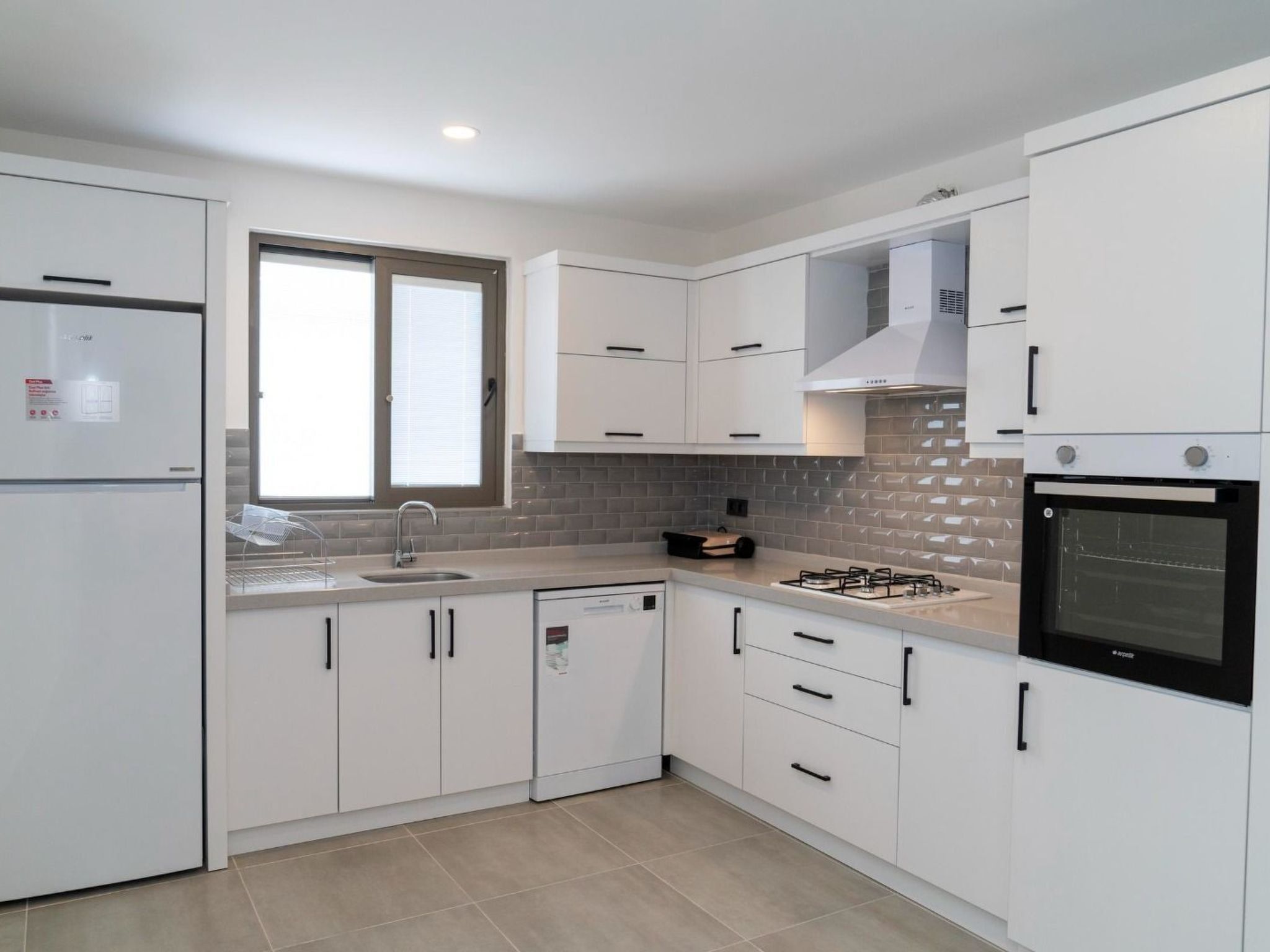 Eine moderne Küche mit weißen Schränken, einem eingebauten Backofen und einem Fenster über der Spüle.