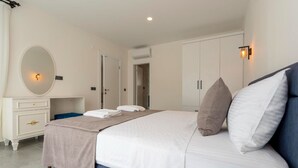 A modern bedroom with a large bed, a dresser, a mirror, and a wardrobe.
