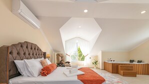 A bedroom with a large bed, a desk, and a view of greenery.