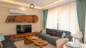 A modern living room with a flat-screen TV, wooden entertainment unit, grey sofa, and a dining area with a table set for two.